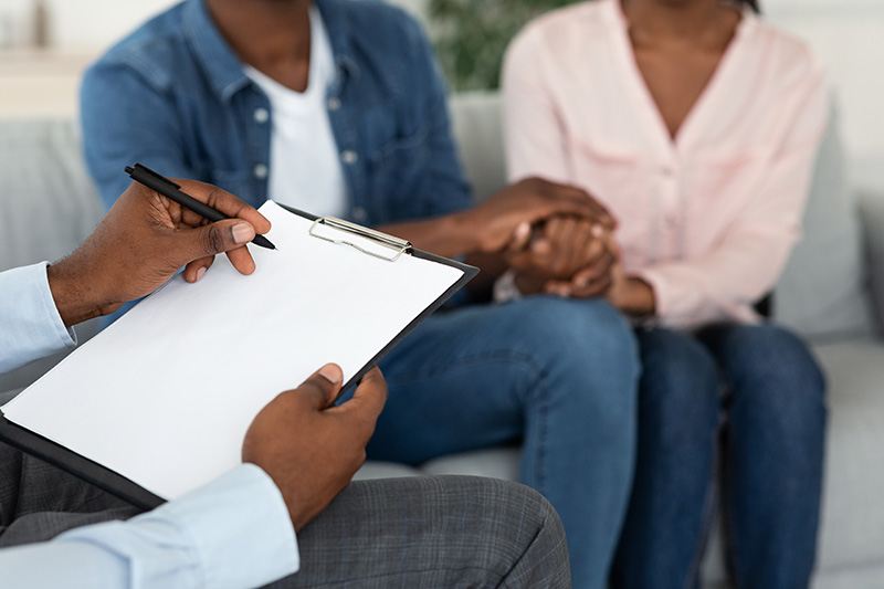 Marital Counselor Taking Notes At Therapy Session With African American Spouses